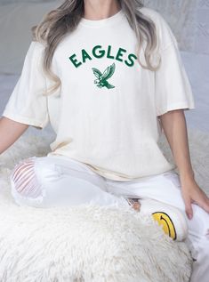 a woman sitting on top of a white sheep wearing an eagle t - shirt with green lettering