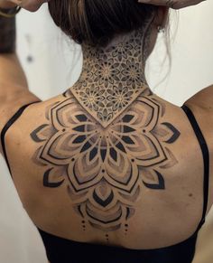 the back of a woman's neck with an intricate tattoo design on her left shoulder