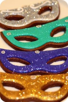 three masks are sitting next to each other on a white plate with gold and blue glitters