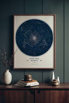 a framed star map hangs on the wall next to a vase with flowers in it