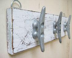 two metal hooks are attached to a white wooden board with rusted paint on it