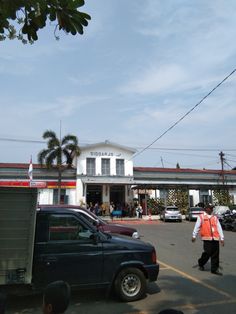 a man in an orange vest is walking towards a building with cars parked on the street