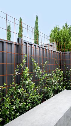 a concrete bench sitting next to a metal fence and shrubbery in front of it