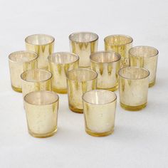 a bunch of glasses sitting next to each other on a white tableclothed surface