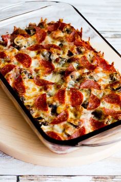 a pizza casserole with pepperoni and mushrooms in a glass dish on a wooden tray