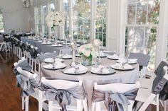 a dining room set up with white and gray table cloths, silver napkins and place settings