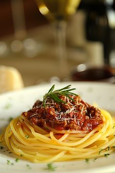 spaghetti with sauce and parmesan cheese on a white plate next to a glass of wine