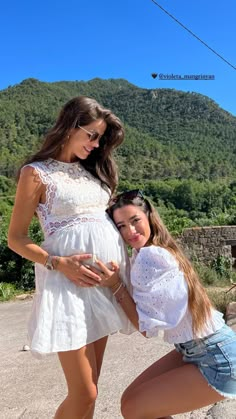 two beautiful young women standing next to each other in front of a green mountain range