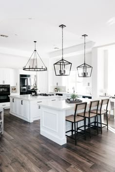 a large kitchen with white cabinets and wood flooring on the walls, along with black pendant lights hanging from the ceiling