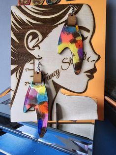 a pair of colorful earrings hanging from a hook in front of a sign that says fancy shop