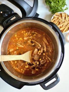 a wooden spoon in a pot filled with soup next to some chips and lettuce