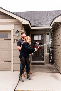 a man and woman standing in front of a house spraying water on them with a hose