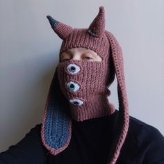 a person wearing a knitted mask with eyes and horns on it's head