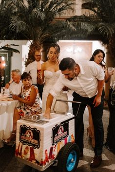 a man and woman cutting into a cake on top of a cart