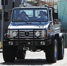 a mercedes benz truck driving down the street with two men sitting in the driver's seat