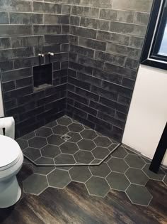 a white toilet sitting in a bathroom next to a shower stall with black tiles on the walls