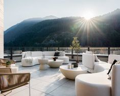 the sun shines brightly on an outdoor patio with white furniture and mountains in the background