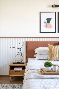 a bed with two pictures on the wall above it and a tray with some plants