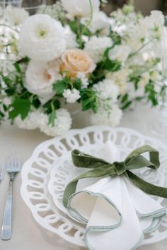 a white plate topped with a bow next to a vase filled with flowers and greenery