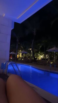 a person sitting next to a swimming pool at night with palm trees in the background