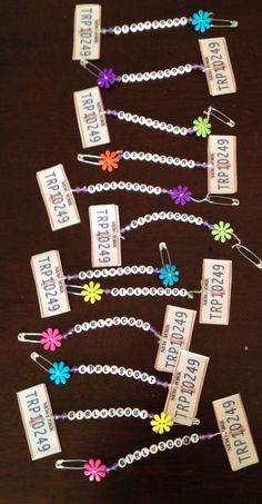 several name tags attached to a chain on a wooden table with flowers and beads around them