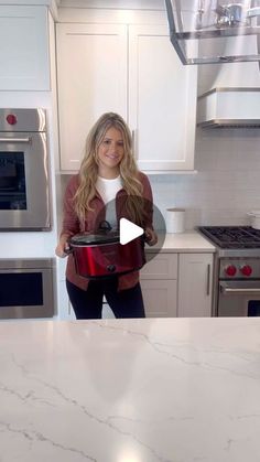 a woman standing in a kitchen holding a pot