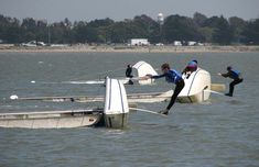 several people on boats in the water with one person falling off their boat and another man jumping off his boat into the water