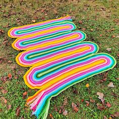 a multicolored blanket laying on the ground with leaves around it and grass in the background