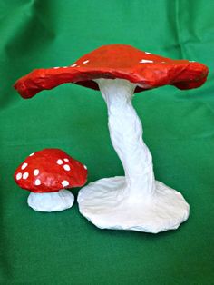 a red and white mushroom sitting on top of a green table next to another mushroom