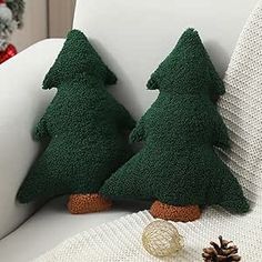 two green christmas trees sitting on top of a white couch next to a pine cone