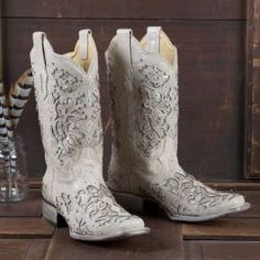 a pair of white cowboy boots sitting on top of a wooden floor next to a vase