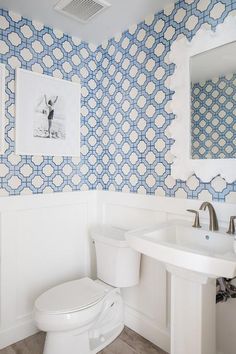 a white toilet sitting under a bathroom mirror next to a sink in a room with blue and white wallpaper