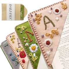 four pieces of fabric with flowers and letters on them are laying next to an open book