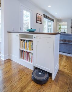 a roomba is sitting on the floor in front of a bookshelf and cabinets