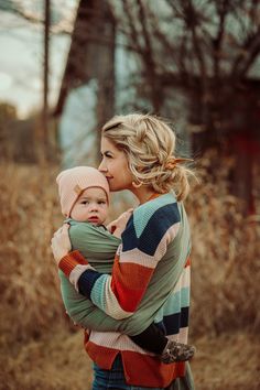 a woman holding a baby in her arms while wearing a striped sweater and matching hat