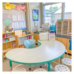 a classroom with several tables and chairs in front of a window that has lots of books on it