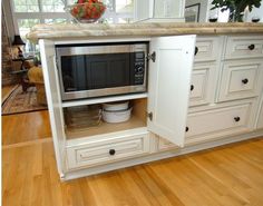 an open cabinet in the middle of a kitchen with white cabinets and wood flooring