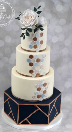 a three tiered cake decorated with flowers and geometric shapes on a plate against a gray background