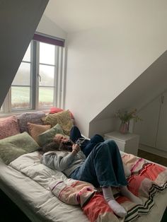 a woman laying on top of a bed next to a window in a room with white walls