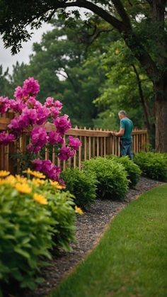 a man standing on a wooden fence next to purple and yellow flowers in a garden