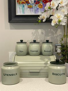 four green canisters sitting on top of a counter next to a vase with white flowers