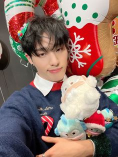 a young man holding a stuffed animal in front of christmas decorations and balloon type balloons