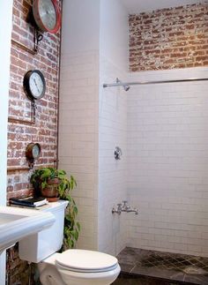 a white toilet sitting in a bathroom next to a sink and shower head mounted on a brick wall