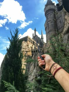 a hand holding a knife in front of a castle with trees and bushes around it