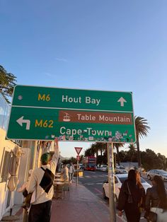 people are standing on the sidewalk next to a street sign that reads m6, hout bay table mountain cape town