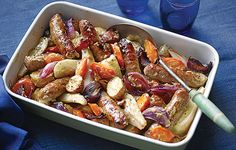 a white dish filled with meat and veggies next to two blue wine glasses