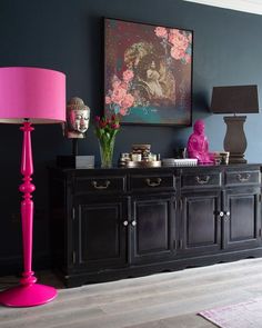 a pink lamp sitting on top of a table next to a black buffet with drawers