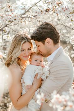 a man and woman are holding a baby in front of some blossoming trees with the sun shining on them