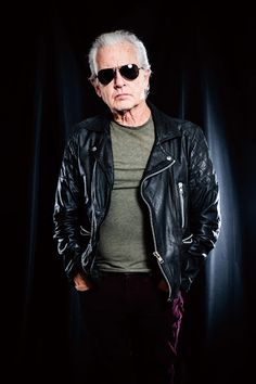 an older man wearing sunglasses standing in front of a black background with his hands on his hips