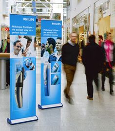 people are walking through an indoor mall with posters on the wall and in front of them